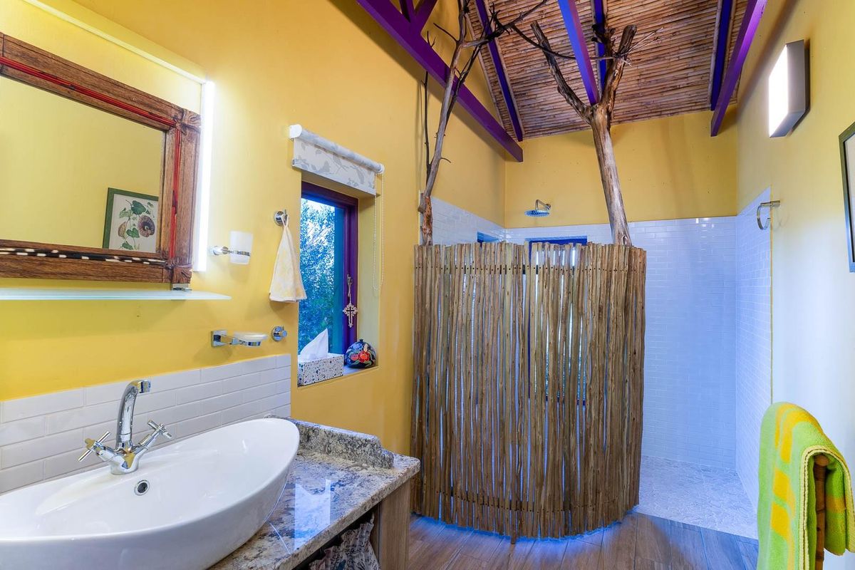 A unique bathroom featuring a vessel sink on a granite vanity, a walk-in shower with a rustic bamboo screen, and a vaulted reed ceiling.