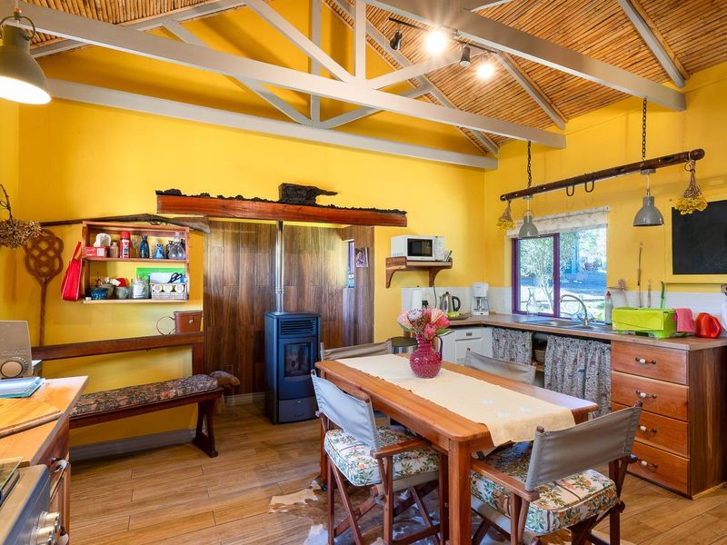 Open-plan kitchen and dining area featuring a wood-burning stove, exposed beam ceiling with bamboo lining, and wooden cabinetry.