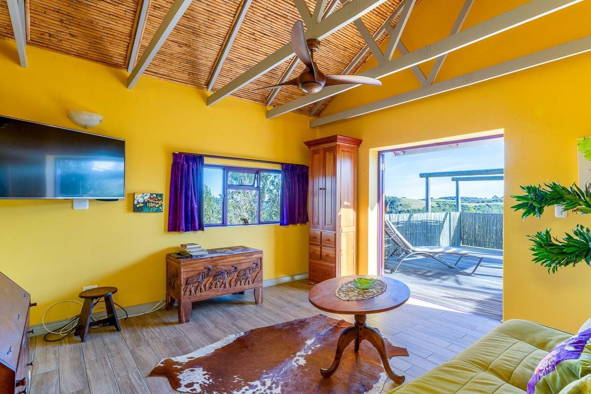 A bright living room featuring a vaulted bamboo ceiling, ceiling fan, and direct access to an outdoor deck with scenic views.