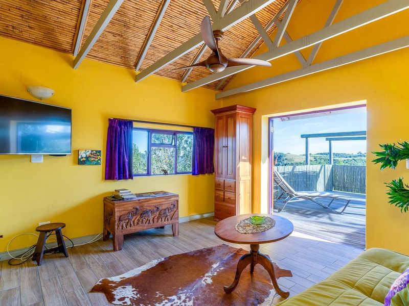 A bright living room featuring a vaulted bamboo ceiling, ceiling fan, and direct access to an outdoor deck with scenic views.
