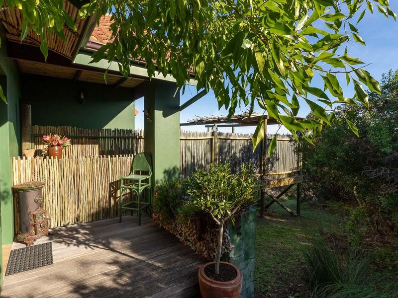 A covered wooden patio area featuring a rustic reed screen, integrated structural pillars, and a view of the surrounding garden landscape.