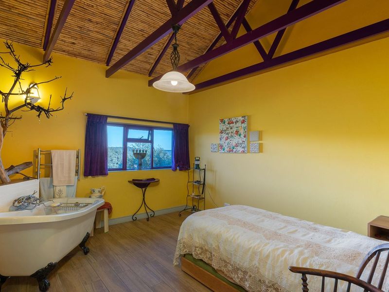 A unique bedroom featuring an open-plan layout with an integrated clawfoot bathtub, vaulted timber-slatted ceiling, and exposed purple-painted roof trusses.