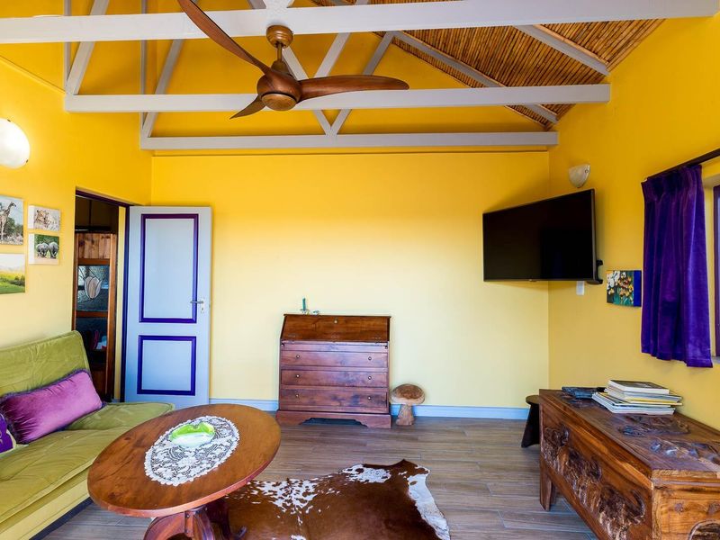 A living room featuring a vaulted ceiling with exposed beams, a ceiling fan, and tiled flooring, offering a bright and functional living space.