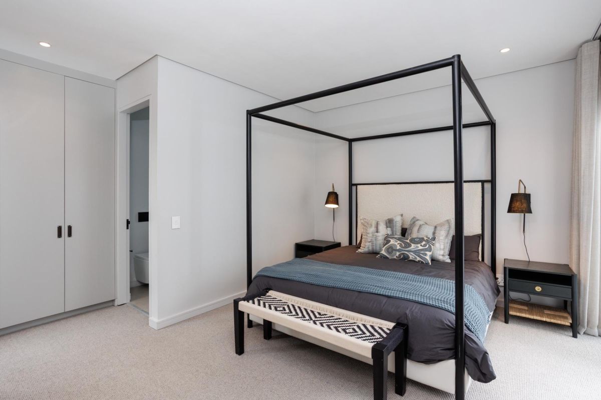 A modern, well-maintained bedroom featuring neutral carpeting, recessed ceiling lighting, and built-in floor-to-ceiling cabinetry, with an adjoining en-suite bathroom.