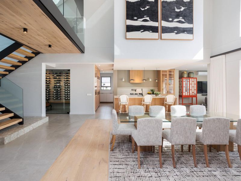 Spacious open-plan living and dining area featuring a modern kitchen, glass-enclosed wine cellar, and a striking floating staircase with timber treads.