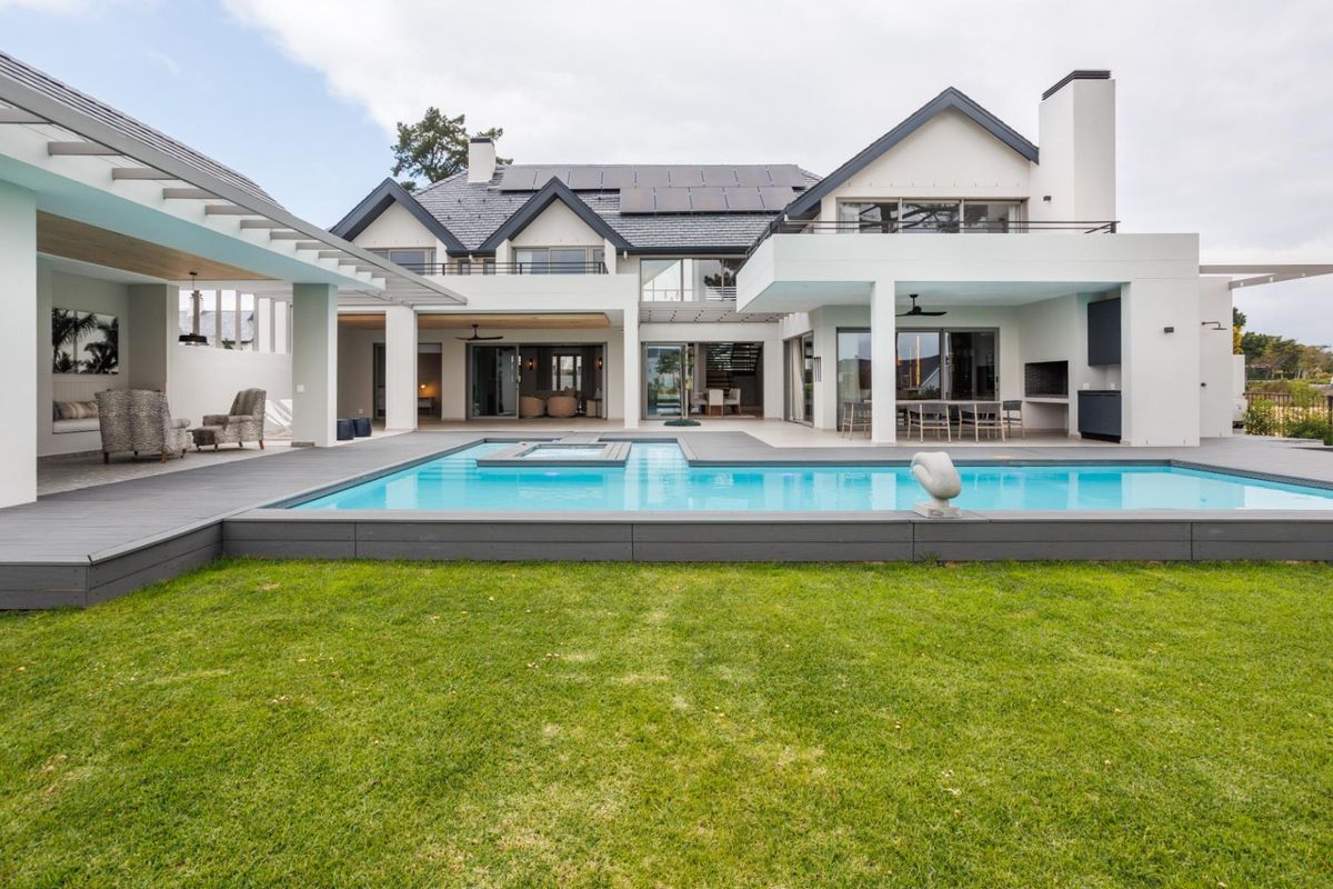 A stunning rear exterior view featuring a modern swimming pool, expansive covered patio, and a beautifully landscaped garden.