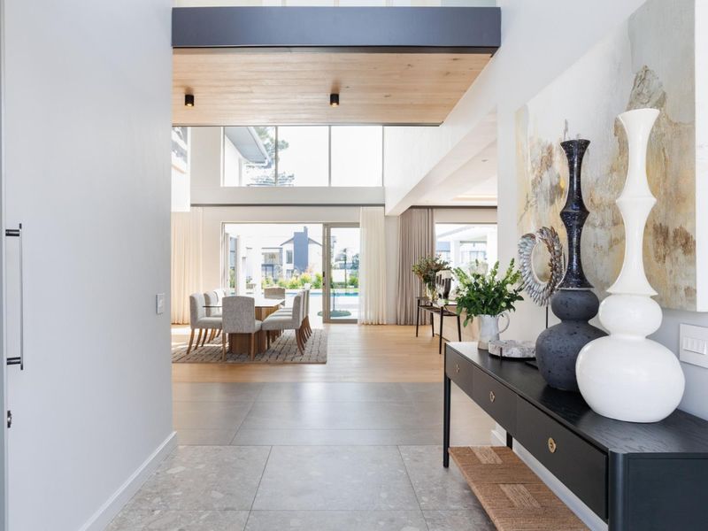 A bright, modern entrance hall leading into a spacious open-plan living and dining area with high ceilings and large glass sliding doors.