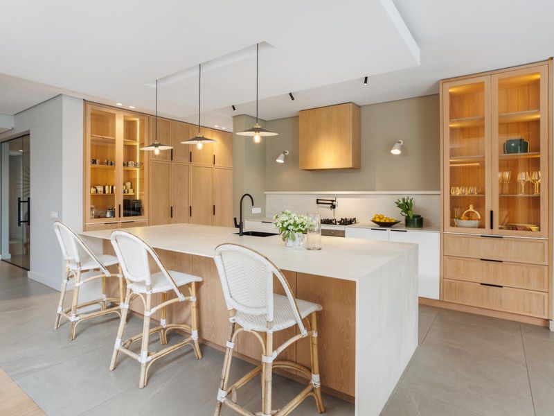 Modern kitchen featuring a large central island with stone countertop, integrated cabinetry, built-in hob, and elegant pendant lighting.