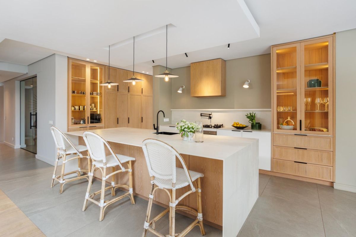 Modern kitchen featuring a large central island with stone countertop, integrated cabinetry, built-in hob, and elegant pendant lighting.