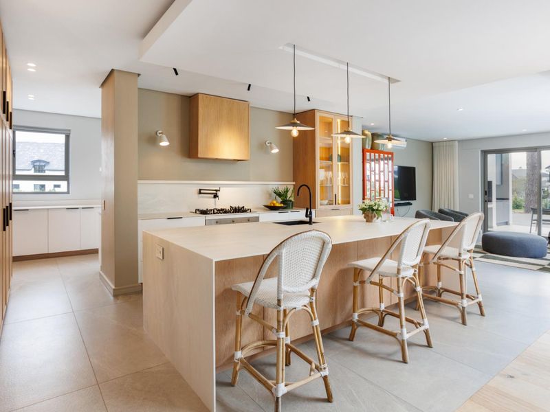 Modern open-plan kitchen featuring a large central island, light wood cabinetry, integrated appliances, and sleek stone countertops, seamlessly flowing into the living area.