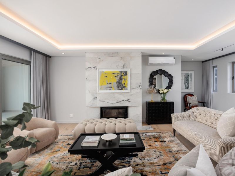 Spacious living room featuring a striking marble-clad fireplace, recessed tray ceiling with ambient lighting, and large sliding glass doors leading to the patio.