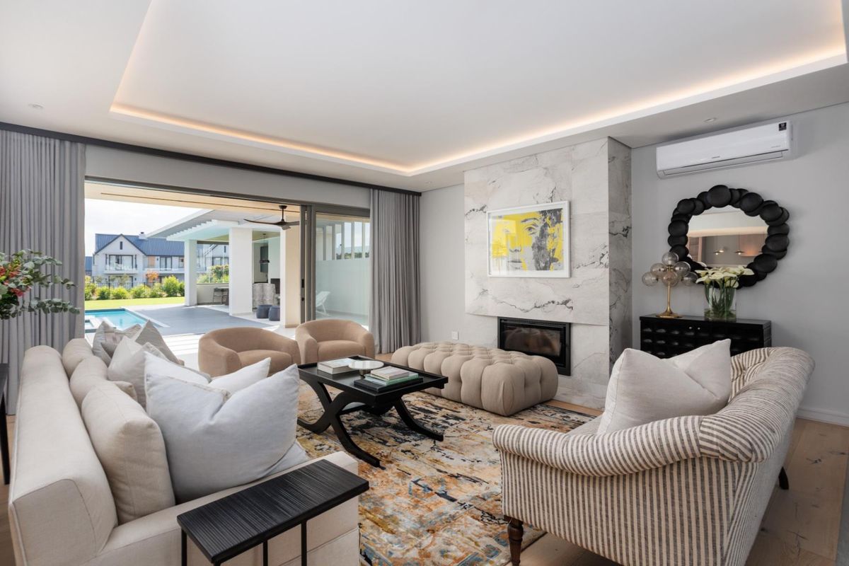 Modern living room featuring a marble-clad fireplace, recessed ceiling lighting, split-system air conditioning, and large sliding glass doors opening to a patio and pool area.