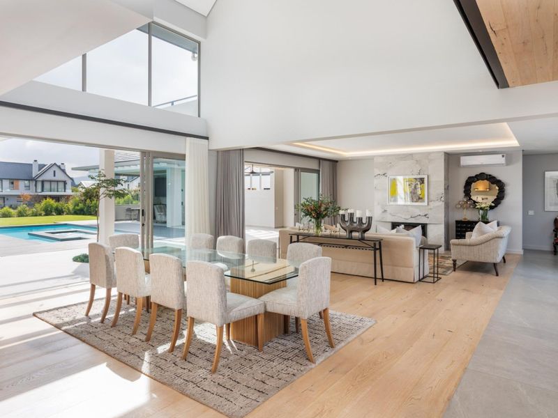 Spacious open-plan living and dining area featuring high ceilings, large glass sliding doors, marble fireplace, and seamless indoor-outdoor flow to the pool area.