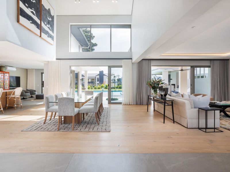 Spacious open-plan living and dining area featuring high ceilings, large windows, light timber flooring, and seamless flow to the outdoor patio and pool area.
