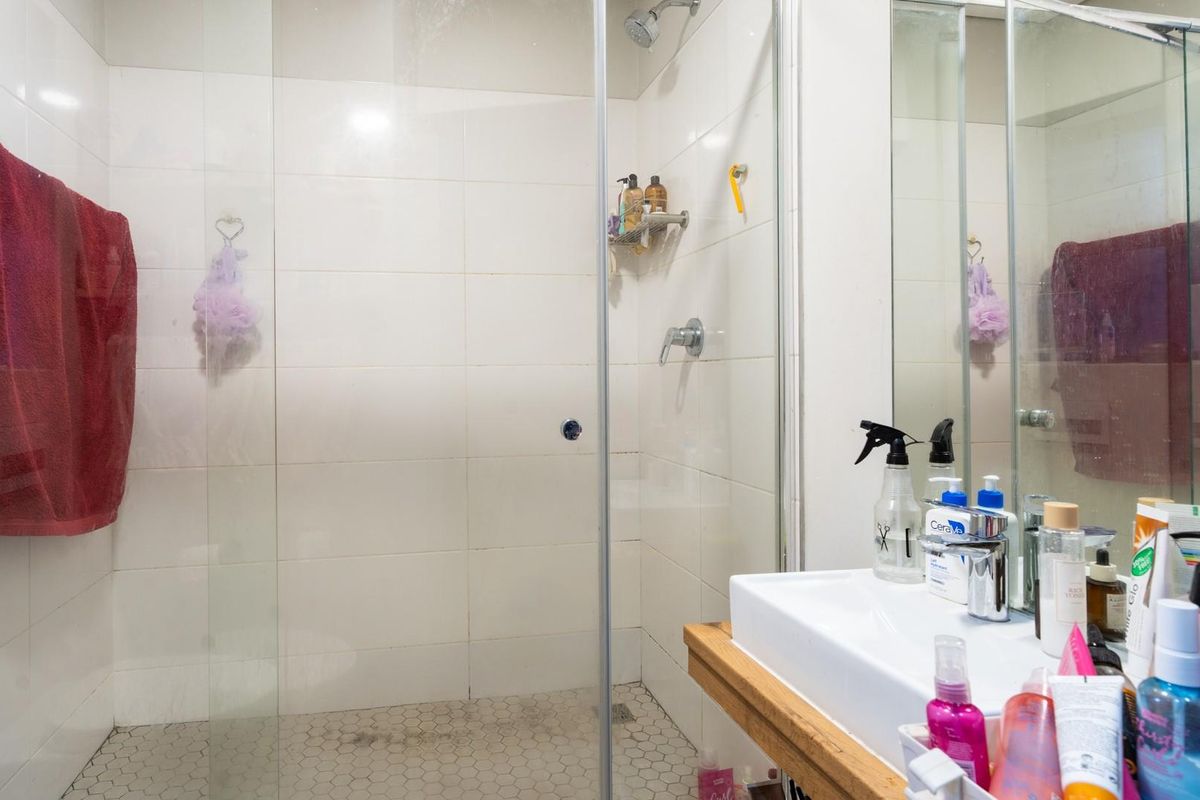 A functional bathroom featuring a glass-enclosed shower with white wall tiles and a modern vanity with a basin.