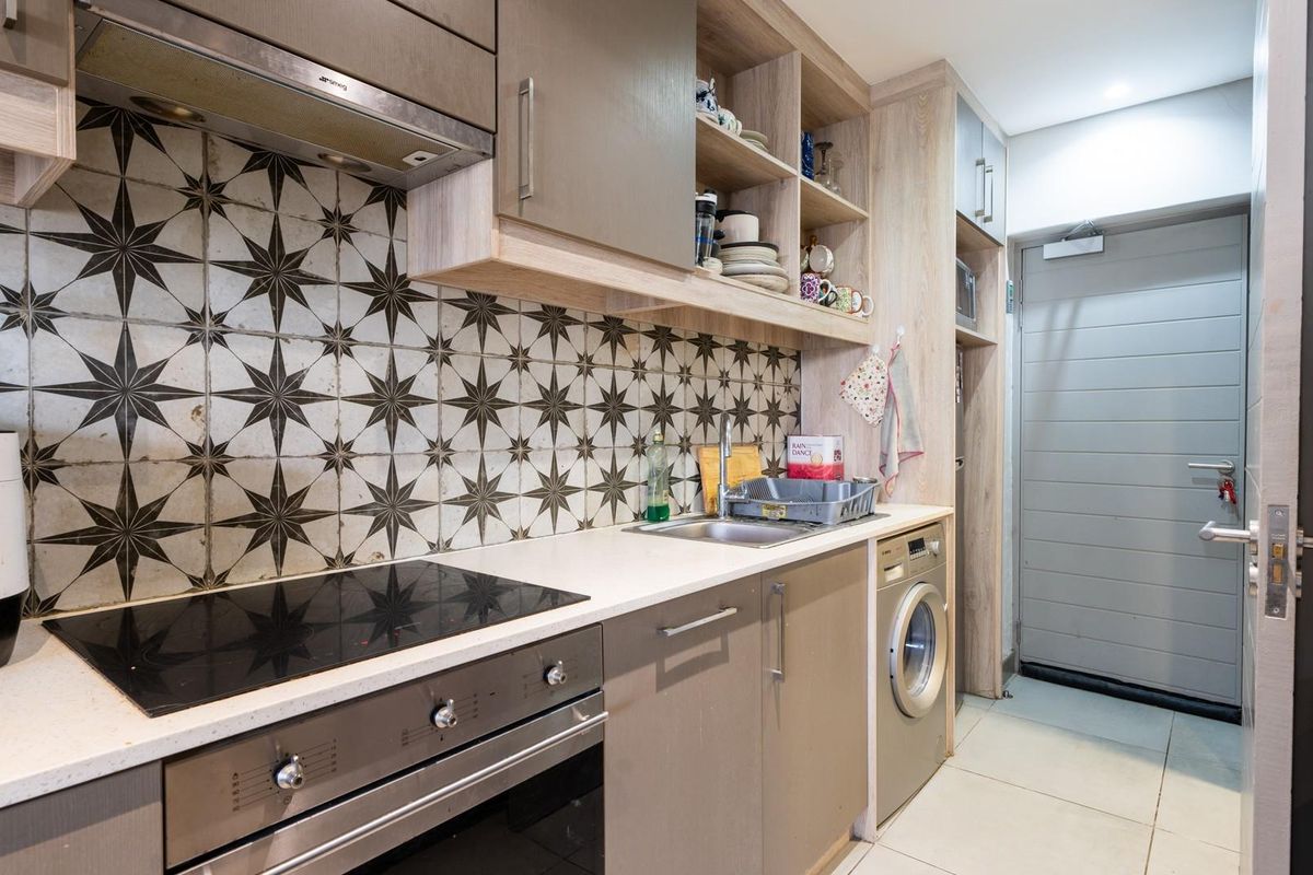 Modern kitchen featuring patterned tile backsplash, integrated oven, electric hob, extractor fan, and built-in laundry appliance space.