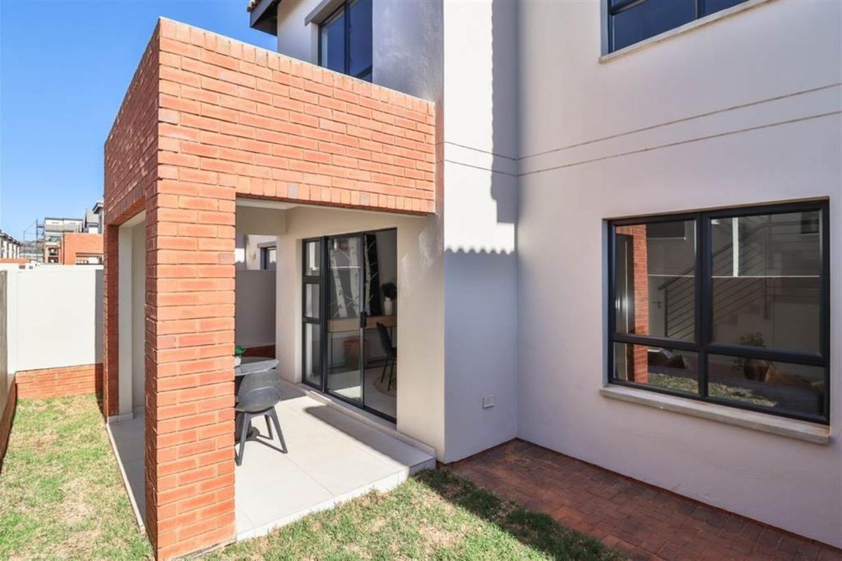 A rear view of the townhouse featuring a covered patio with exposed brick pillars, tiled flooring, and sliding glass doors leading to the interior.