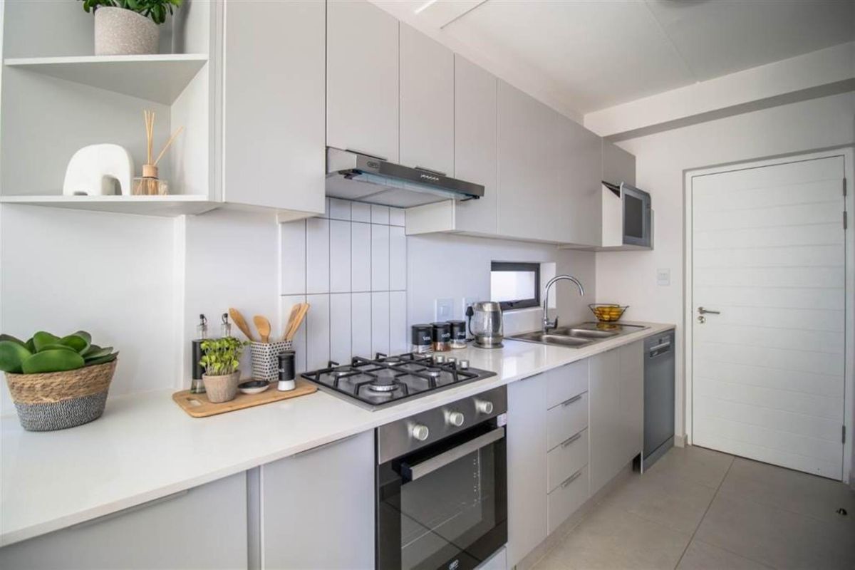 Modern kitchen featuring light grey cabinetry, white countertops, a built-in gas hob, oven, extractor fan, and a double sink with tiled splashback.