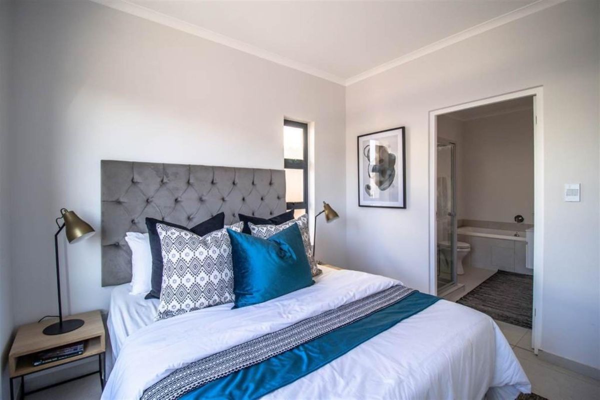 A well-lit bedroom featuring neutral walls, tiled flooring, and an en-suite bathroom with a shower and bathtub.