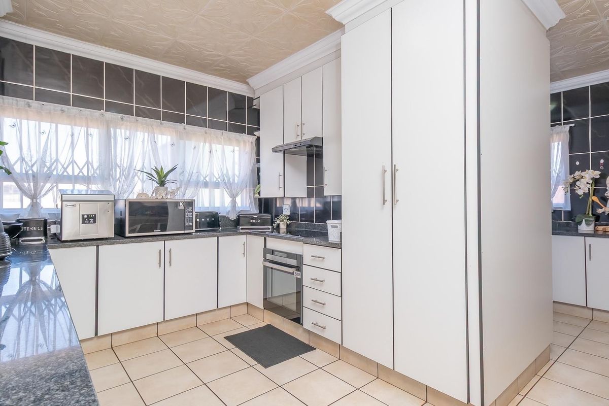 A functional kitchen featuring white cabinetry, dark granite countertops, built-in oven, extractor fan, and tiled flooring with a classic layout.
