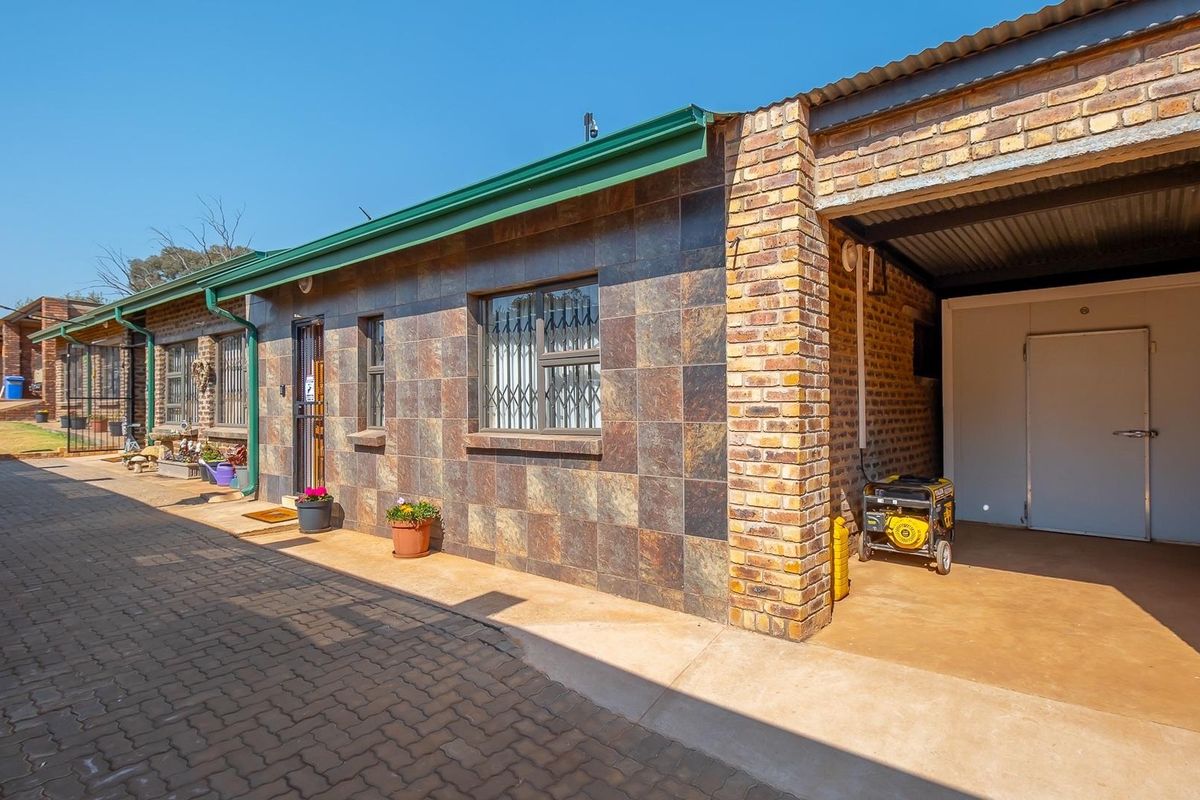 Exterior view of a farm building featuring tiled facade, brick pillars, paved walkway, and a covered utility area with a secure door.
