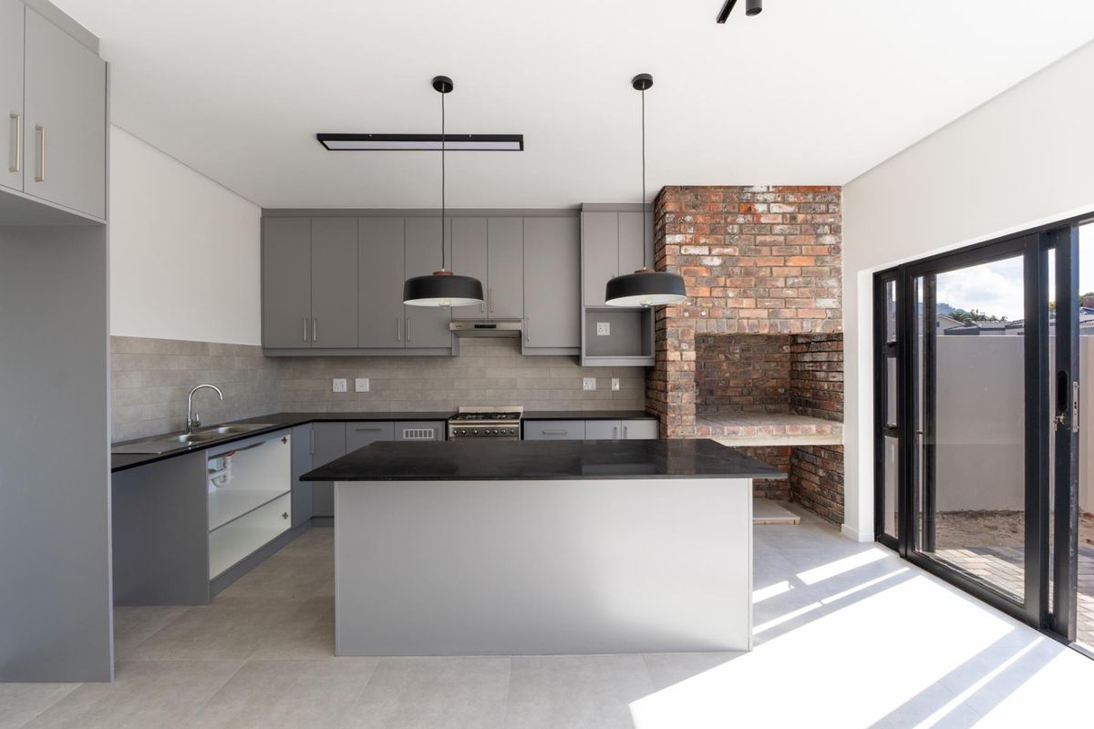 Modern kitchen featuring grey cabinetry, stone countertops, a central island, built-in oven, and an integrated brick fireplace, with direct access to the outdoor area.