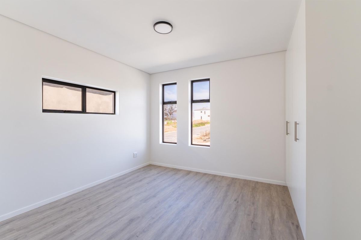 A bright, modern, and empty bedroom featuring neutral wood-look flooring, clean white walls, and built-in cabinetry.