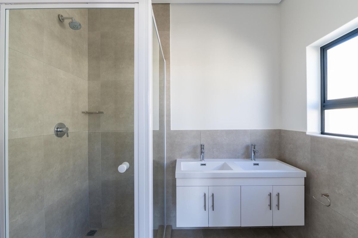 Modern bathroom featuring a double vanity with white cabinetry, a glass-enclosed shower with neutral wall tiling, and a window for natural light.