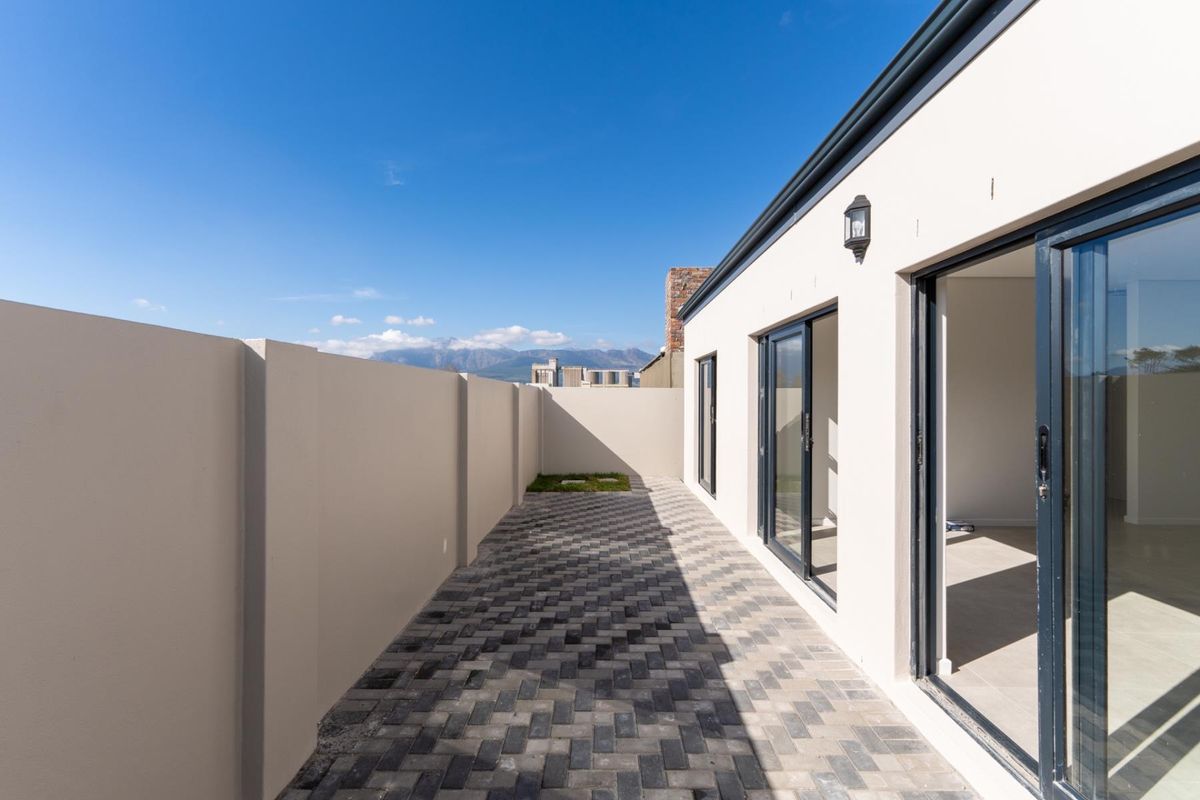 A paved rear courtyard area featuring a high boundary wall, modern sliding glass doors, and exterior wall-mounted lighting.