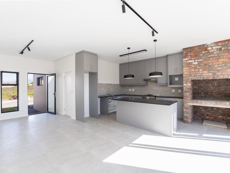 Modern open-plan kitchen featuring grey cabinetry, stone countertops, integrated oven and hob, and a rustic exposed brick indoor fireplace.