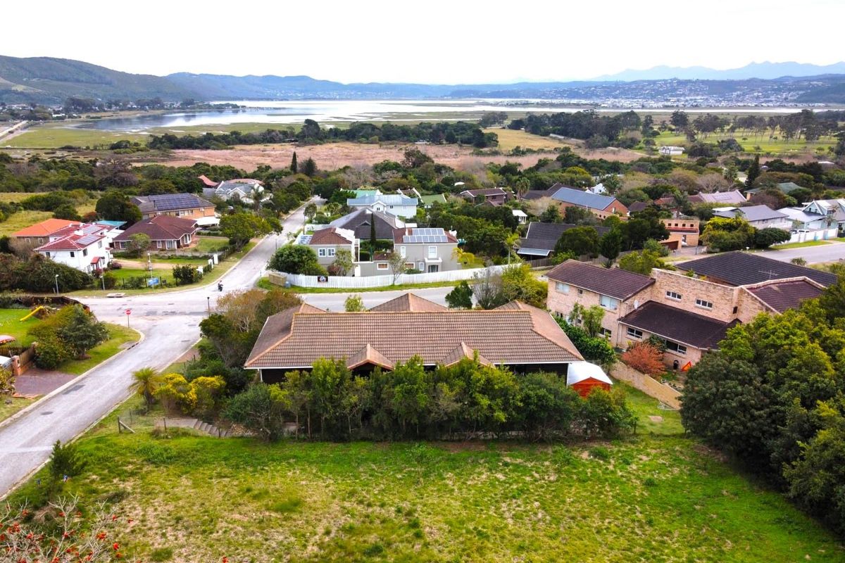 An elevated aerial view of a residential property lot, showcasing the surrounding neighborhood, local landscape, and distant water views.