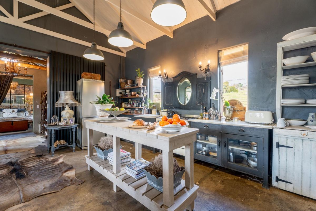 A rustic-style kitchen featuring exposed vaulted ceilings, dark cabinetry, a central island, and polished concrete flooring with an open-plan layout.