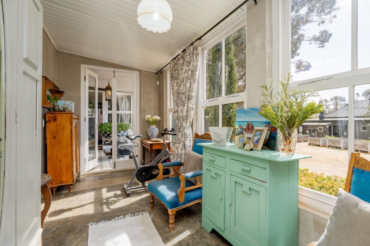 A sun-drenched sunroom featuring large windows, concrete flooring, and double glass doors leading to an adjacent living space.