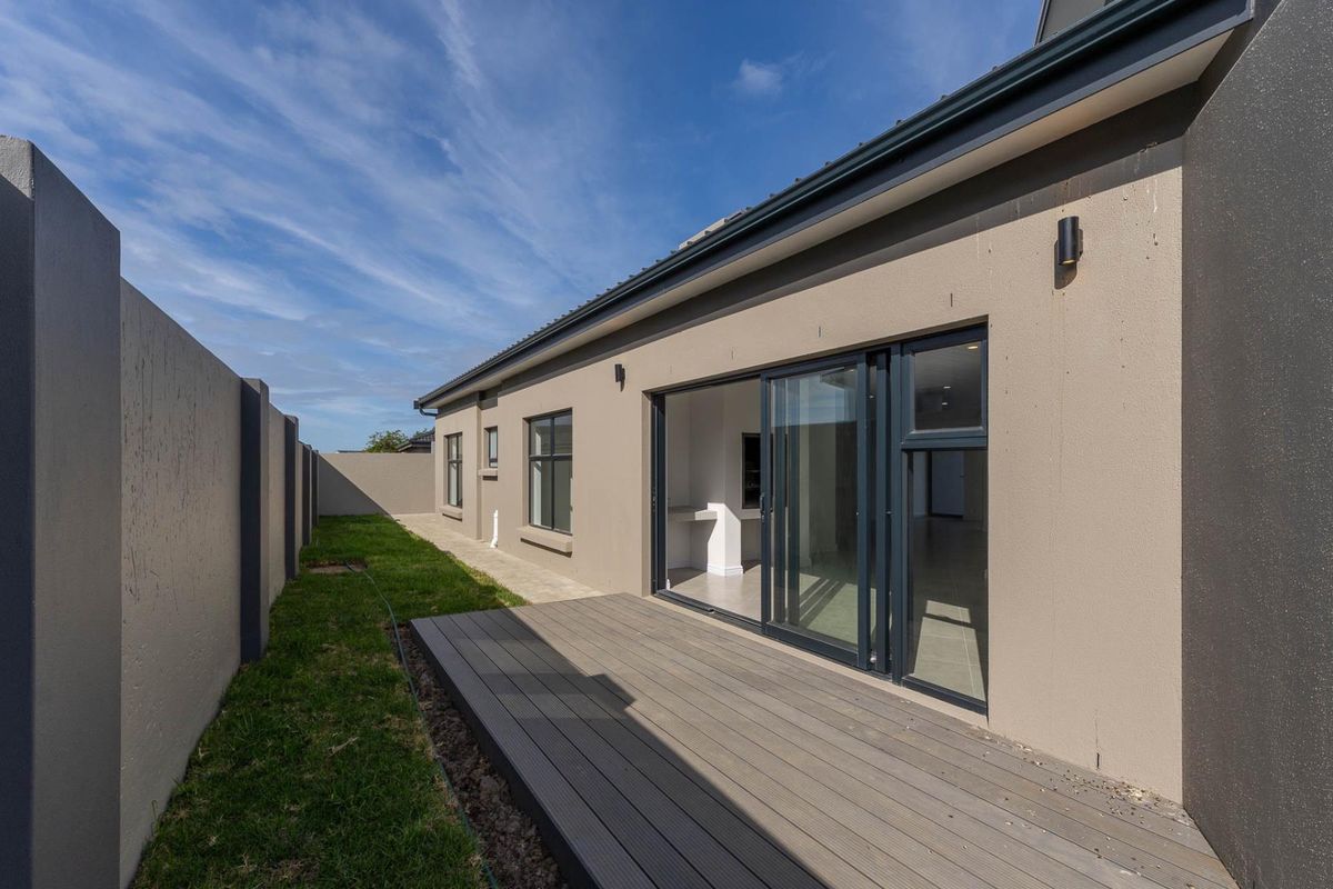 Rear view of the property featuring a composite deck, sliding glass doors, and a private garden area with perimeter walling.