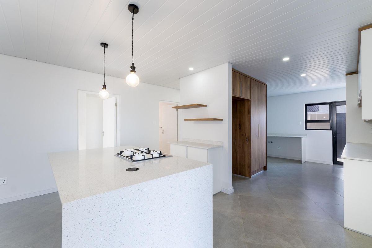 Modern open-plan kitchen featuring a central island with a built-in gas hob, stone countertops, and sleek wood-grain cabinetry.
