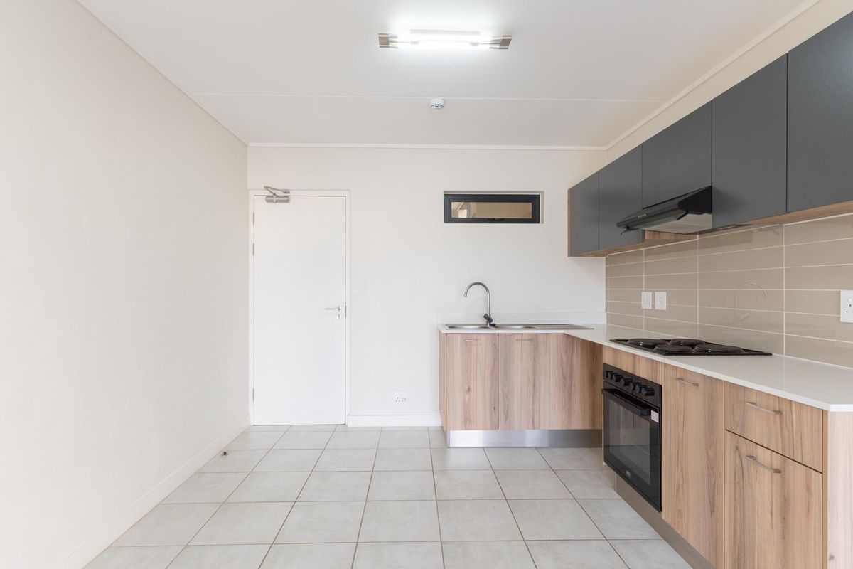 Modern kitchen featuring light wood-look cabinetry, dark grey overhead cupboards, built-in oven, hob, extractor fan, and neutral tiled flooring.