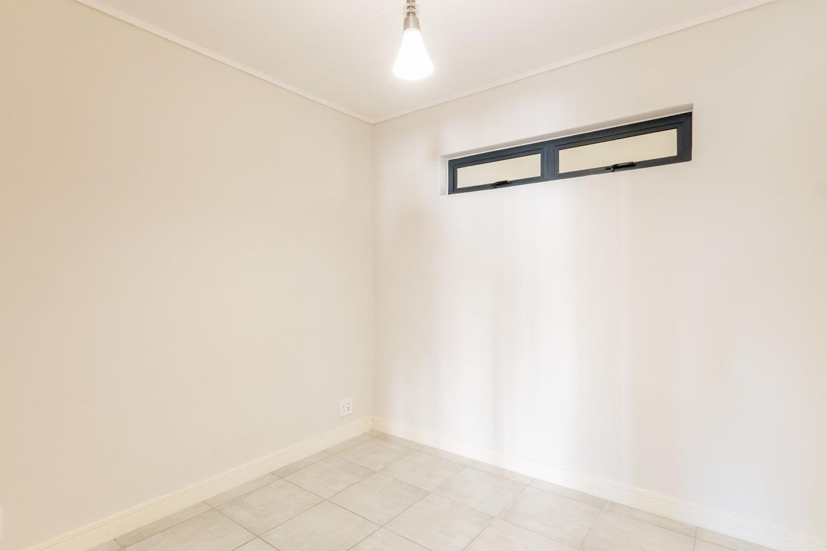 A clean, empty bedroom featuring neutral tiled flooring, a high-level horizontal window, and simple pendant lighting, ready for personalization.