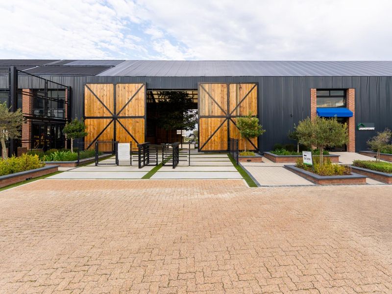 Modern industrial-style apartment complex entrance featuring large timber barn doors, corrugated metal facade, and landscaped brick planter boxes.