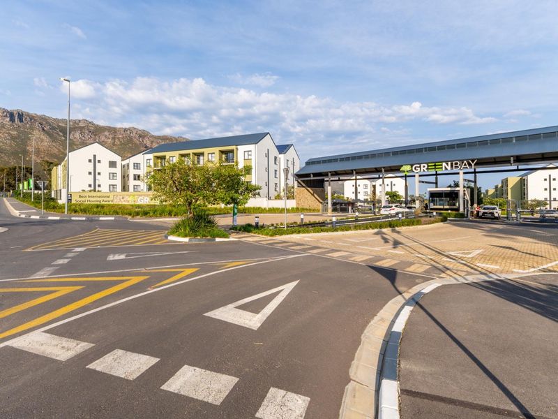 View of the Greenbay apartment complex entrance, featuring a modern security gatehouse, paved access roads, and well-maintained landscaped surroundings.