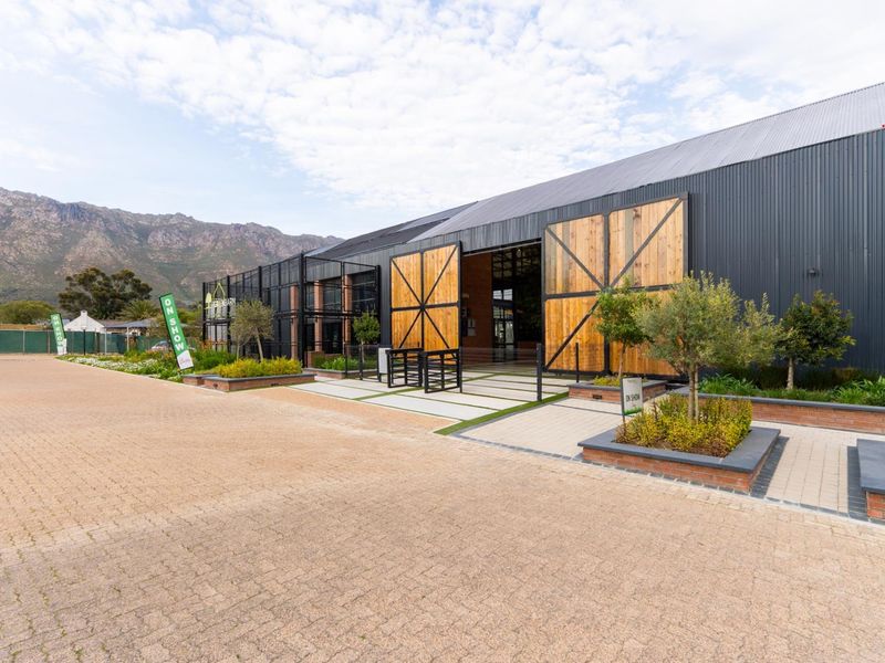 Modern industrial-style building facade featuring large timber barn doors, corrugated metal cladding, and landscaped brick planters with a paved driveway.