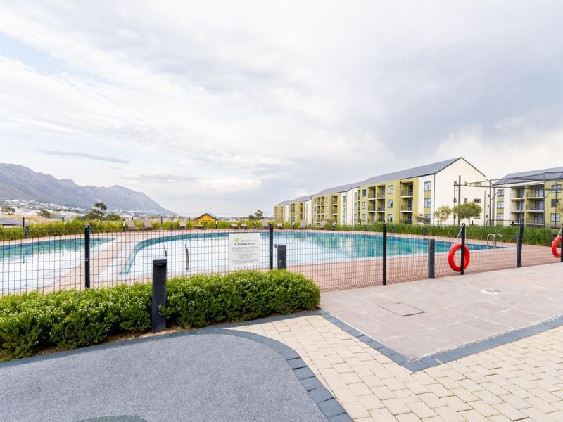 Communal swimming pool area featuring paved surrounds, perimeter fencing, and mountain views within a well-maintained apartment complex.