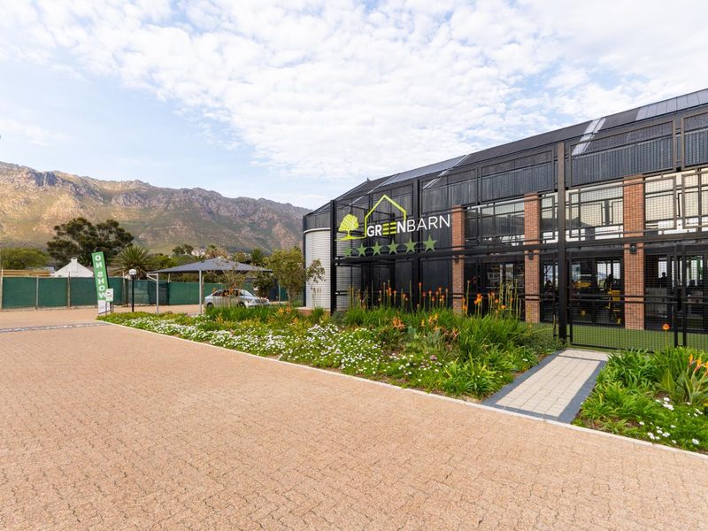 Modern exterior facade of the Greenbarn building featuring industrial metal mesh detailing, brick accents, and well-maintained landscaped garden beds.