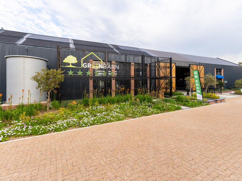 Modern industrial-style building exterior featuring dark metal cladding, integrated solar panels, a water tank, and well-maintained landscaped gardens.