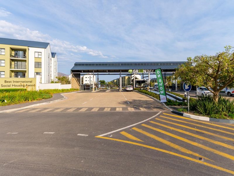 The entrance to the Greenbay residential complex, featuring a modern security gatehouse, paved driveway, and well-maintained landscaping.