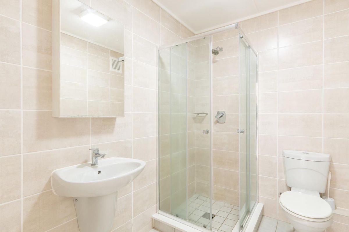 A clean and functional bathroom featuring a pedestal washbasin, a glass-enclosed shower, and a wall-mounted mirror cabinet with neutral wall tiling.