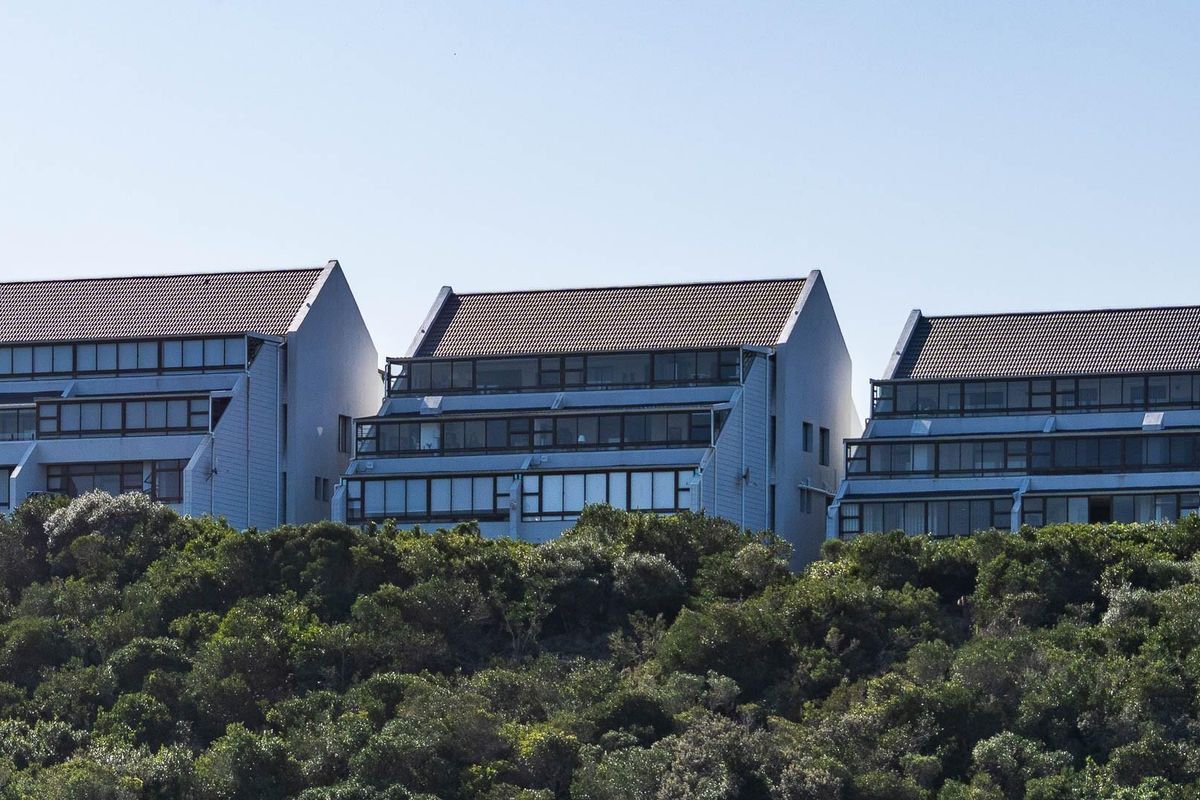 A view of a multi-story apartment complex featuring tiered balconies and tiled roofing, set against a backdrop of dense coastal vegetation.