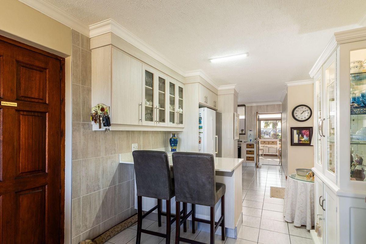 A functional kitchen area featuring light-toned cabinetry, a breakfast bar, and tiled flooring, leading through to an adjacent living space.