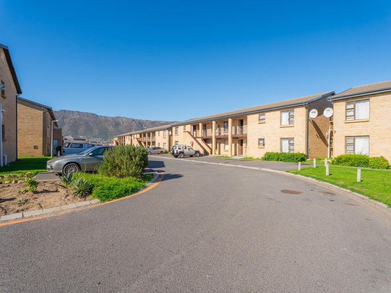 Exterior view of a multi-unit apartment complex featuring brick facades, paved driveways, and mountain views in the background.