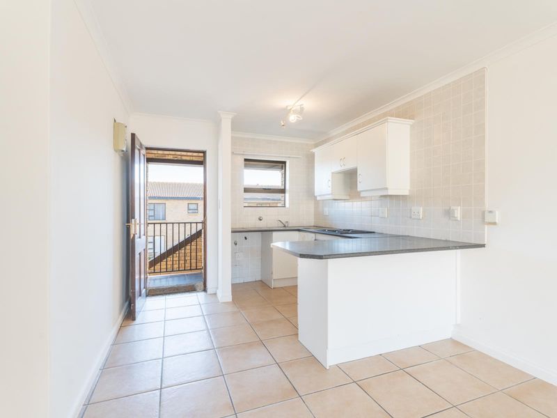 A clean, functional kitchen featuring white cabinetry, dark laminate countertops, tiled backsplash, and a breakfast bar, with direct access to an outdoor balcony.