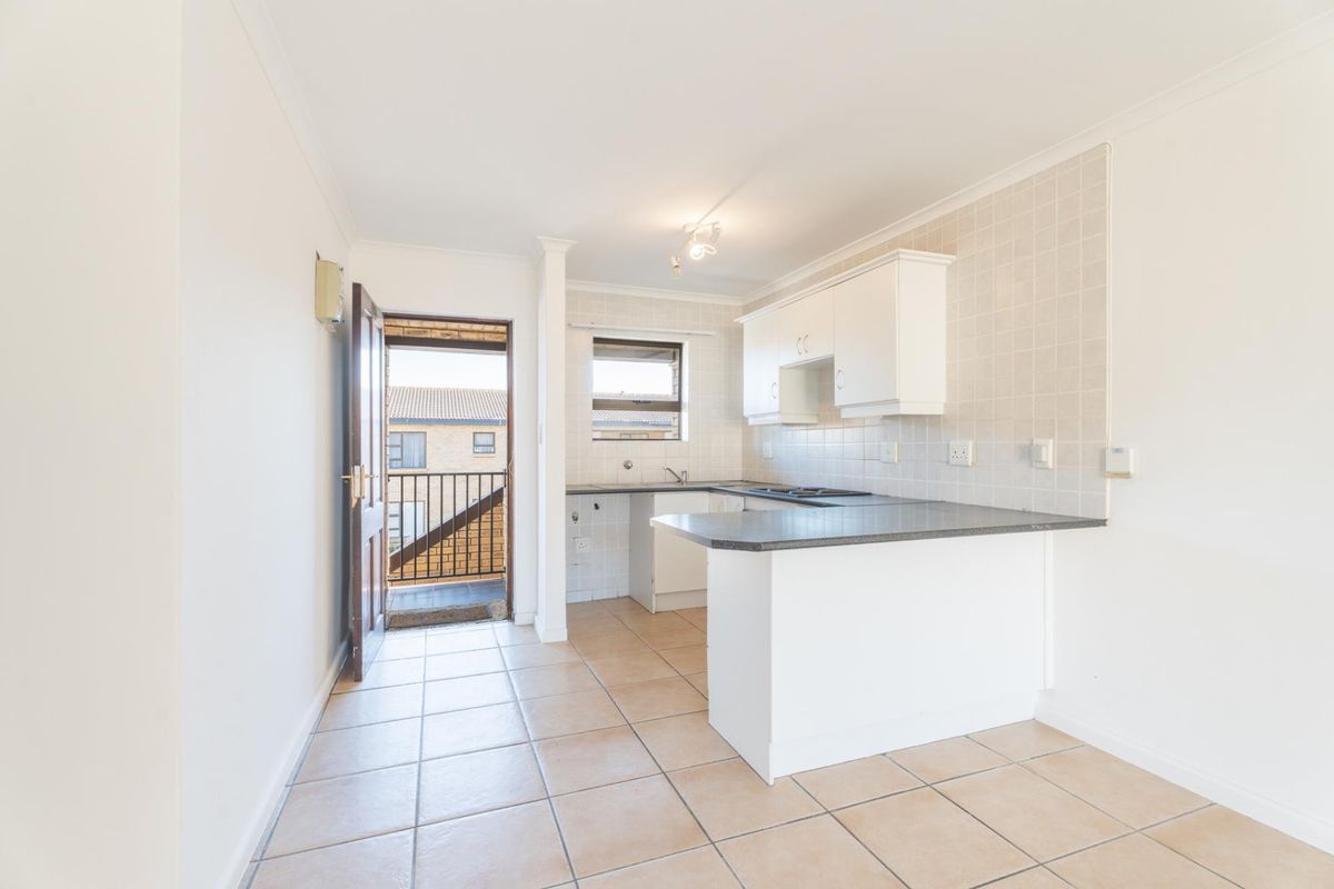 A clean, functional kitchen featuring white cabinetry, dark laminate countertops, tiled backsplash, and a breakfast bar, with direct access to an outdoor balcony.